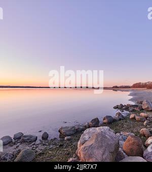 Ruhige, ruhige und abgelegene Landschaft mit Blick auf den Strand und das Meerwasser während des Sonnenuntergangs im Sommer. Schöne, ruhige und malerische Aussicht auf das Meer und die Küste Stockfoto