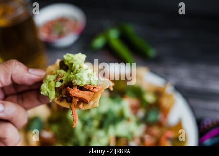 Hand hält mexikanische Nacho-Chips mit amerikanischem Käse und Avocado, traditionelles Essen in Mexiko Lateinamerika Stockfoto