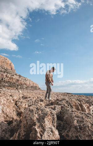 Der junge Mann springt auf einem Wüstenboden vor dem Berg Cape Greco Stockfoto