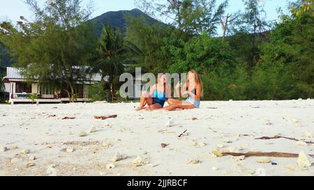Zwei kaukasische Freundinnen sitzen an einem Strand und unterhalten sich in Koh Phangan, Thailand Stockfoto