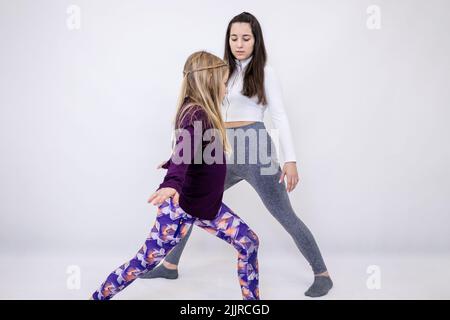 Junge attraktive Yogalehrerin und ihre kleine Schülerin machen beim Training intensive Bewegungen Stockfoto