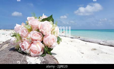 Eine Nahaufnahme von Strauß rosa Rosen am Sandstrand im Hintergrund Meer Stockfoto