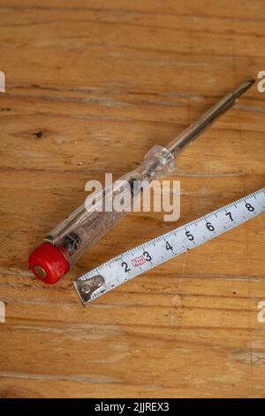 Eine vertikale Aufnahme eines alten elektrischen Spannungsprüfers und weißes Messband auf einem Holztisch Stockfoto