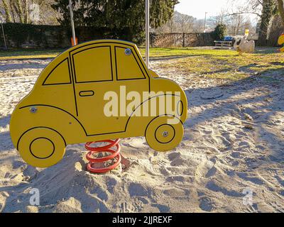 Eine Nahaufnahme einer Frühlings-Wippe in Form eines Autos auf dem Spielplatz mit Sandboden Stockfoto