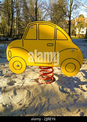 Eine vertikale Aufnahme einer Frühlings-Wippe in Form eines Autos auf dem Spielplatz mit sandigen Boden Stockfoto