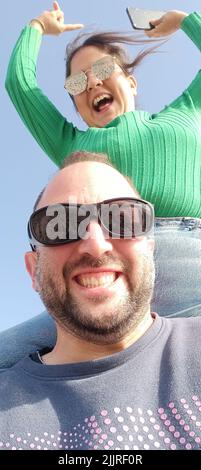 Eine vertikale Aufnahme eines glücklichen Reisenden Paares, das Selfie gegen einen blauen Himmel macht Stockfoto