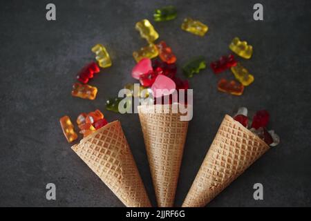 Ein Blick von oben auf drei Waffelkegel mit bunten Gelees auf einer grauen Oberfläche Stockfoto