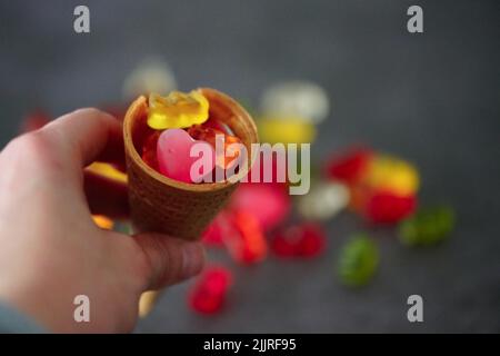Eine Nahaufnahme einer Hand, die einen Waffelkegel mit bunten Gelees auf der Oberseite hält Stockfoto