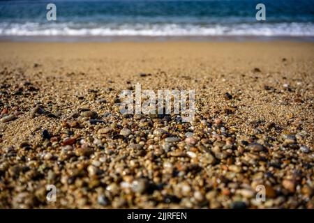 Nahaufnahme eines felsigen und sandigen Strandes mit türkisfarbenen Meereswellen im Hintergrund Stockfoto