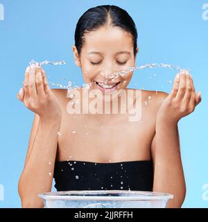 Es gibt keinen falschen Weg, um Ihren Körper zu lieben. Eine schöne junge Frau spritzt Wasser auf ihr Gesicht vor einem blauen Hintergrund. Stockfoto