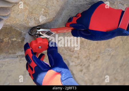 Männliche Hände in Arbeitshandschuhen, die den Hahn mit einem Schraubenschlüssel nach außen reparieren Stockfoto