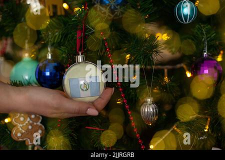 Ein Mädchen hält eine Dekoration auf einem Weihnachtsbaum mit der Flagge Guatemalas Stockfoto