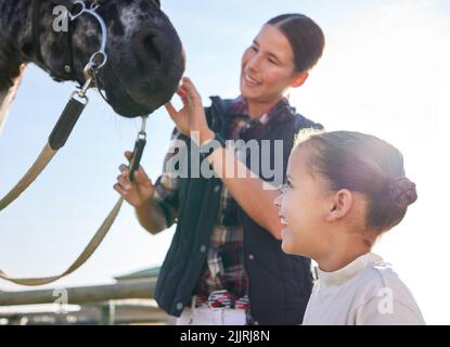 Siehe Hes Friendly. Eine attraktive junge Frau und ihre Tochter streicheln ein Pferd draußen auf der Ranch. Stockfoto