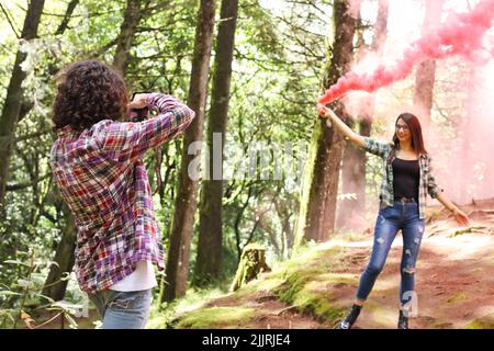 Anonymer professioneller Fotograf, der in Costa Rica ein Model mit einer roten Rauchbombe im Wald fotografiert Stockfoto