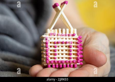 Ein kleines Streichholz-Haus in den Händen einer alten Frau, ein hausgemachtes Haus aus Streichhölzern Stockfoto