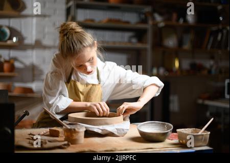 Ein Keramiker macht einen Teller. Frau in einer Schürze arbeitet in einer Töpferwerkstatt. Stockfoto