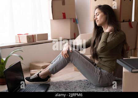 Erschöpfte junge hispanische Frau sitzen zu Hause Boden massiert Nackengefühl Schmerzen, müde Mädchen leiden unter Rückenschmerzen oder Belastung, mit Krämpfen Symptome Stockfoto