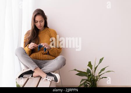 Häkeln von Frauen. Handarbeit. Häkelnadel. Weibliche Hände halten einen Haken und stricken einen Schal. Handarbeit stricken. Heimhobby Stockfoto