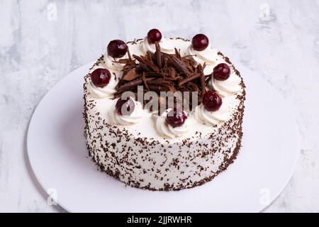 Eine Nahaufnahme von weißer Creme auf Schwarzwälder Tortenkuchen mit Kirschen auf weißer Marmoroberfläche Stockfoto
