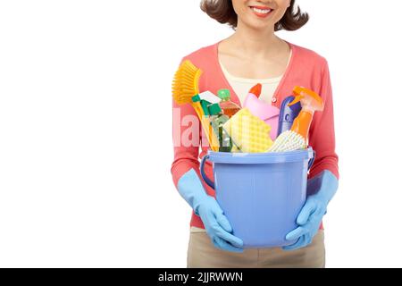 Nahaufnahme einer lächelnden Hausfrau, die Eimer mit Reinigungsutensilien in den Händen hält, während sie vor weißem Hintergrund steht Stockfoto