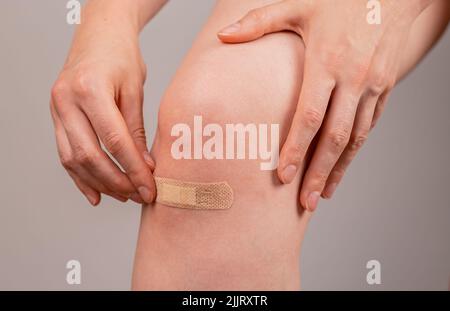 Frau, die medizinischen Gips auf das Knie aufgetragen hat. Erste-Hilfe-Konzept. Schnitte, Abschürfungen und leicht blutende Wunden heilen. Infektionsprävention. Hochwertige Fotos Stockfoto