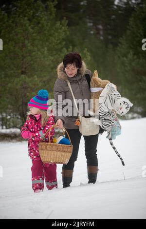 Ein süßes Mädchen in einem rosa Overall und eine Frau in einem Wintermantel mit Spielzeug in einem verschneiten Park Stockfoto