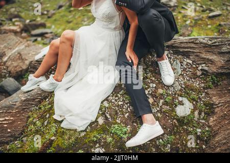 Halbkörperansicht eines verliebten Ehepaars in weißen Schuhen, das auf einem Felsen in den Bergen sitzt. Natur, Reisen, Ruhe. Stockfoto