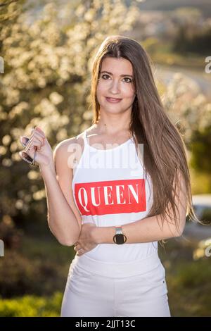 Eine vertikale Aufnahme einer jungen Frau mit langen Haaren, die in der Nähe eines blühenden Baumes im Garten posiert. Frühlingstag. Parfüms und Mode Stockfoto