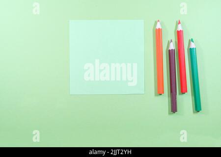 Eine Draufsicht auf Minze-Haftnotizen mit Copyspace neben bunten Bleistiften auf hellgrünem Hintergrund Stockfoto