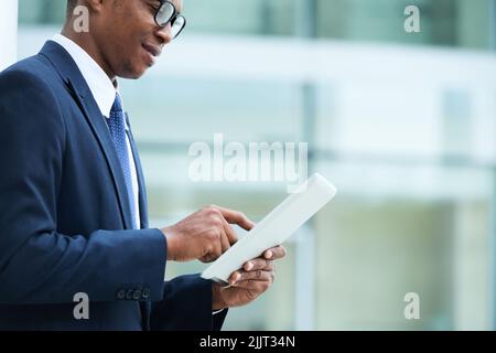 Zugeschnittenes Bild eines afroamerikanischen Geschäftsmannes, der wichtige Dokumente online liest Stockfoto