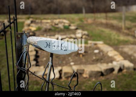 Ein Schild mit der Aufschrift „Kräuter“ auf einem eisernen Zaun vor dem Hintergrund eines Gemüsegartens Stockfoto