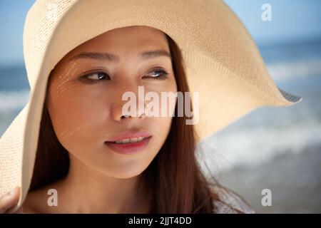 Gesicht einer hübschen asiatischen jungen Frau, die Strohhut am Strand trägt Stockfoto
