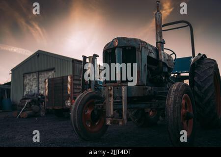 Ein Bild eines alten rostigen Traktors mit einem Logo auf einem Bauernhof unter dem Abend glühenden Himmel Stockfoto