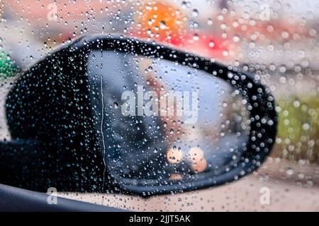 Eine Nahaufnahme eines Seitenspiegels, der durch das Autoglas mit Regentropfen darauf gesehen wird Stockfoto