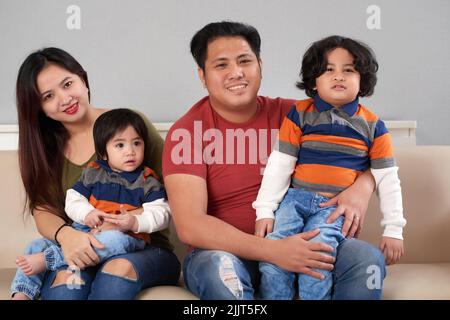 Glückliche philippinische vierköpfige Familie sitzt auf dem Sofa Stockfoto