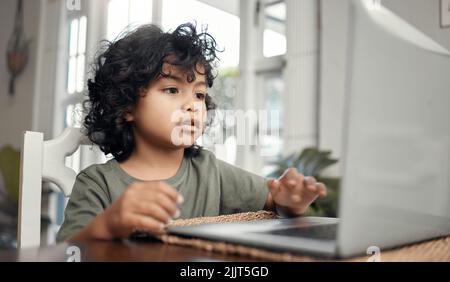 Ich bin sicher, dass ich das lösen kann. Ein entzückender kleiner Junge, der einen Laptop benutzt, während er zu Hause sitzt. Stockfoto