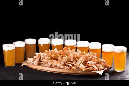 Bierset für eine große Gruppe von Freunden. Bier in Gläsern in Nahaufnahme auf dem Betontisch. Bier und Snacks sind knusprige Chips auf einem Holztablett. Stockfoto