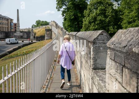 City of York antike römische Mauern, weibliche blonde Touristenmodell freigegeben Spaziergang entlang der Umfassungsmauer, York, Yorkshire, England Sommer 2022 Stockfoto