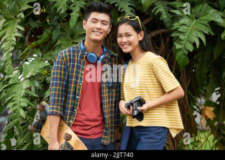 Fröhliches vietnamesisches junges Paar mit Skateboard und Digitalkamera Stockfoto