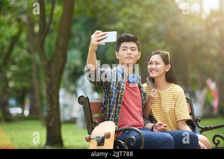 Glückliches asiatisches junges Paar, das im Park zusammen fotografiert Stockfoto