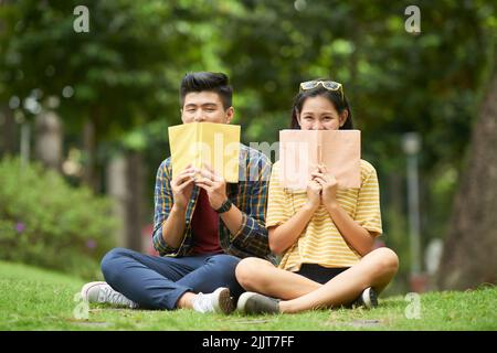 Fröhliche Studenten mit Büchern, die im Park sitzen Stockfoto