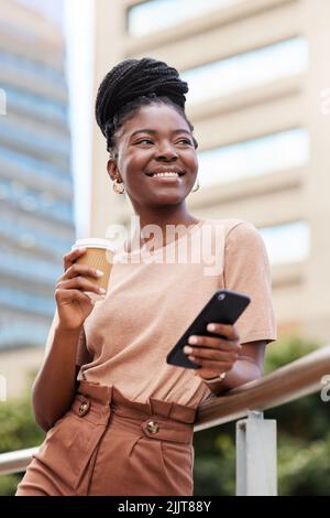 Halten Sie Ihren Fokus immer nach vorne. Eine junge Geschäftsfrau, die draußen auf dem Balkon steht und ihr Handy benutzt, während sie eine Tasse Kaffee hält. Stockfoto
