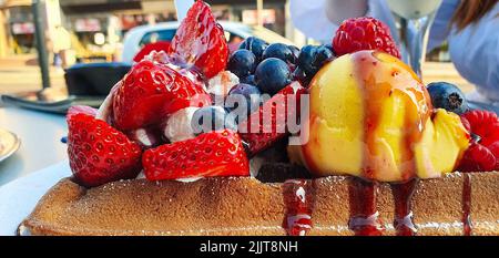 Eine Waffel, die mit Eis mit Beeren und Erdbeeren bedeckt ist Stockfoto