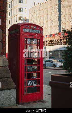 Eine vertikale Aufnahme einer roten Telefonzelle in London, Großbritannien, in der sonnigen Straße im Freien Stockfoto