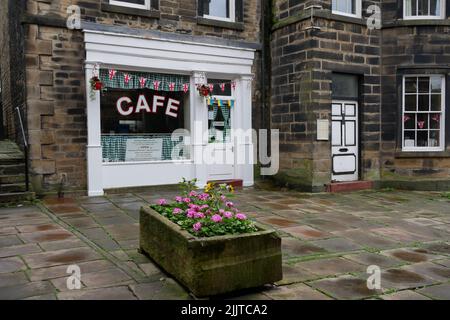 Café mit weißer Eingangstür und Fenstern, umgeben von Steinboden-Fassade und Blumentopf Stockfoto