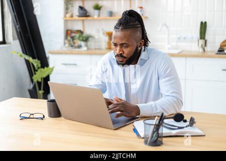 Konzentrierter afroamerikanischer Freiberufler mit Laptop-Computer, der von zu Hause aus arbeitet Remote Work Stockfoto