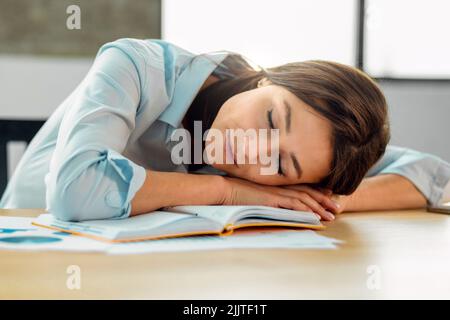 Porträt einer müden jungen Frau, die am Arbeitsplatz in der Büroarbeit eingeschlafen ist Stockfoto