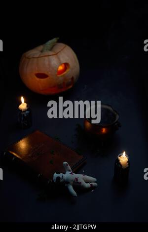 Halloween Kürbis mit brennendem Mund, Buch und einer Voodoo Puppe - Volt auf dunklem Hintergrund. Halloween-Konzept. Stockfoto