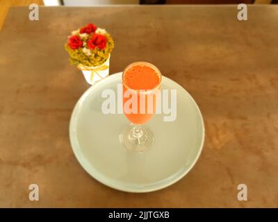 Ein Blick von oben auf ein Glas Erdbeermilchshake auf weißem Teller neben Blumen auf dem Tisch Stockfoto