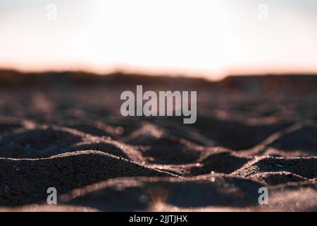 Eine Aufnahme des Strandsands im niedrigen Winkel während des Sonnenuntergangs auf Bokeh-Hintergrund Stockfoto